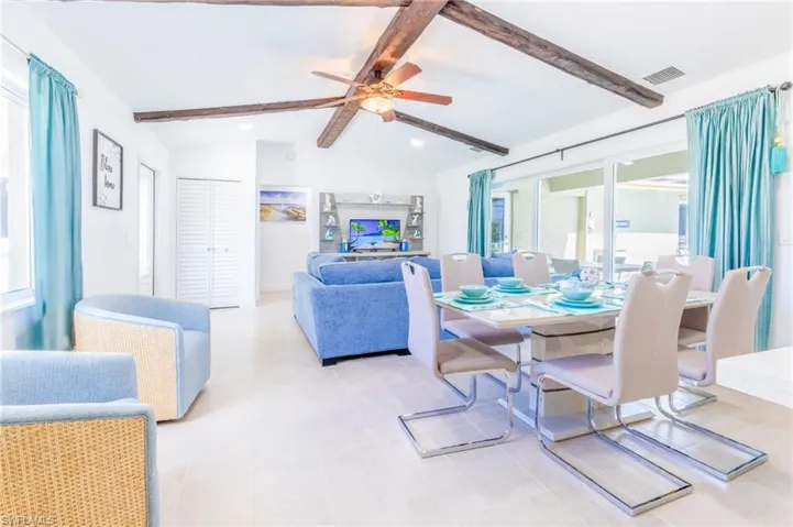 Open-concept living area featuring vaulted ceilings with exposed wood beams, tile flooring, and sliding glass doors providing access to outdoor spaces