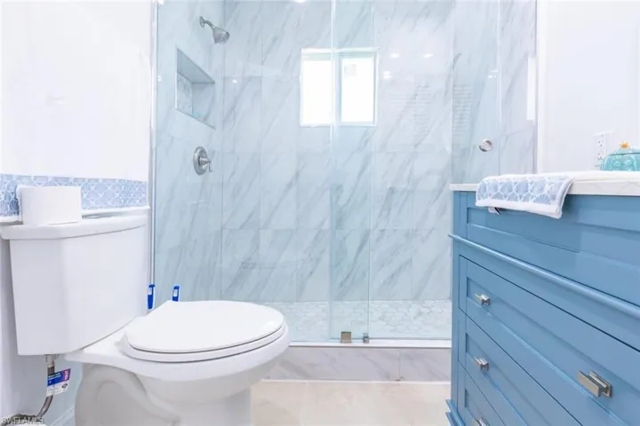 Glass-enclosed shower with large format marble-look tile, pebble-tile shower floor, and a built-in shower niche