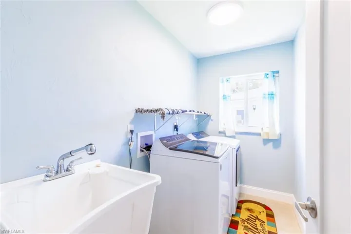 Dedicated laundry area featuring a utility sink with a chrome pull-out faucet, a window providing natural light, and tile flooring