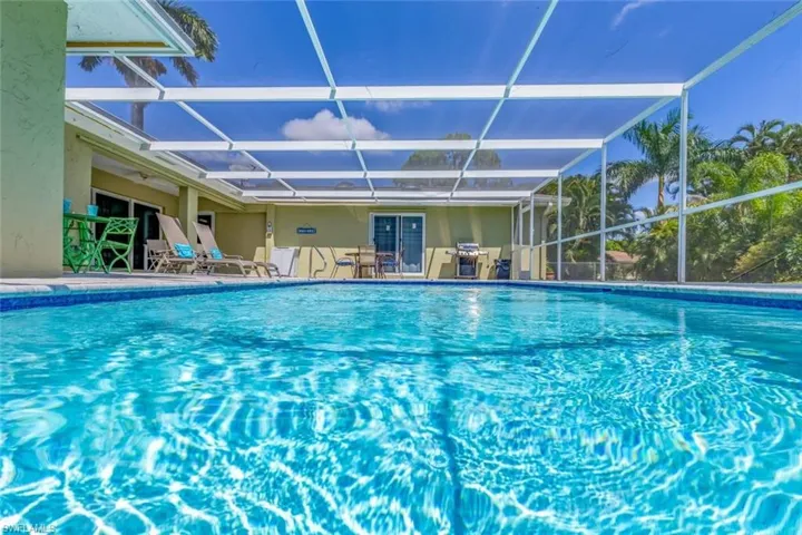Screened swimming pool enclosure featuring a blue-tiled pool, expansive pool deck, and lush tropical landscaping