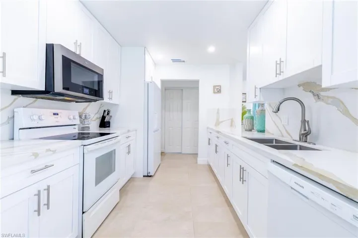 Contemporary kitchen featuring white cabinetry, light-toned countertops with a subtle vein pattern, a stainless steel microwave, a dual basin sink, and tile flooring