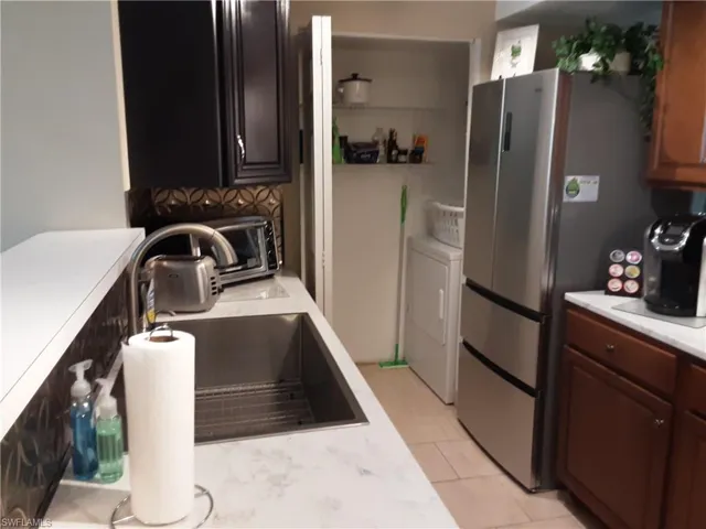 Kitchen with washing machine and clothes dryer, a sink, light tile patterned flooring, light countertops, and freestanding refrigerator
