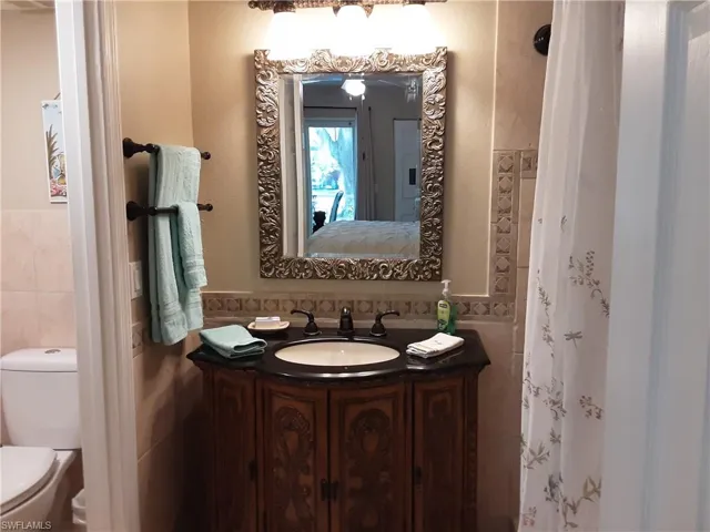 Ensuite bathroom featuring toilet, vanity, tile walls, a wainscoted wall, and ensuite bath