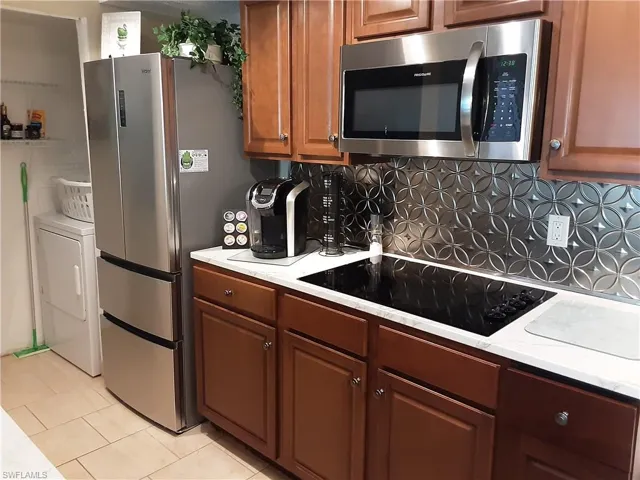 Kitchen with brown cabinets, stainless steel appliances, backsplash, light tile patterned floors, and washer / dryer