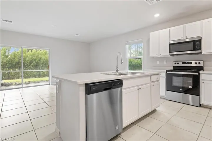 Kitchen featuring stainless steel appliances, light tile patterned flooring, white cabinets, a kitchen island with sink, and recessed lighting