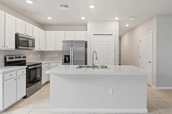 Kitchen with stainless steel appliances, a center island with sink, white cabinets, light tile patterned floors, and recessed lighting