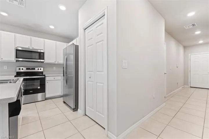 Kitchen with recessed lighting, stainless steel appliances, light tile patterned floors, white cabinets, and light stone countertops