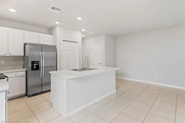 Kitchen with stainless steel fridge, an island with sink, white cabinets, light tile patterned floors, and recessed lighting