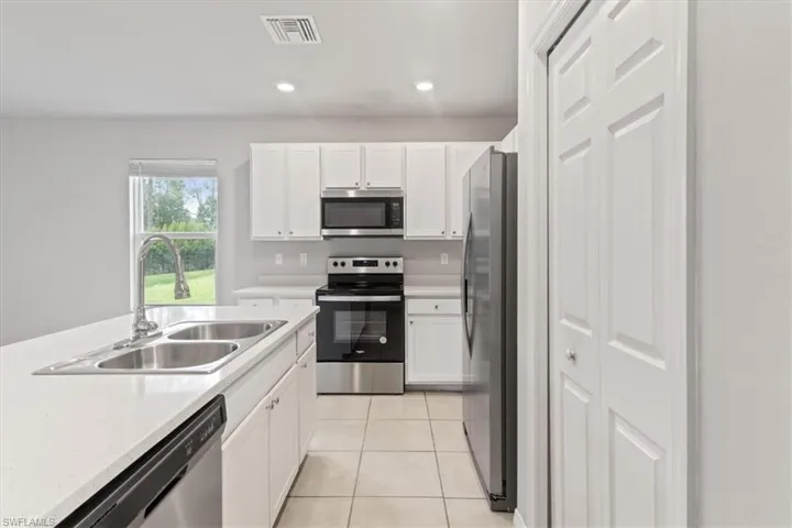 Kitchen with stainless steel appliances, white cabinets, light tile patterned flooring, and recessed lighting
