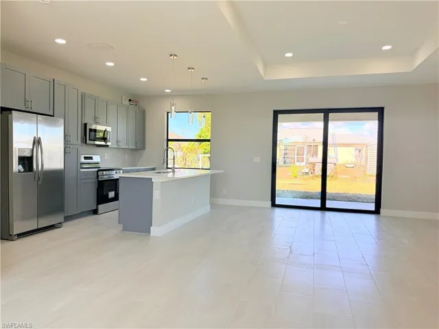 Kitchen featuring stainless steel appliances, decorative light fixtures, gray cabinets, plenty of natural light, and a tray ceiling