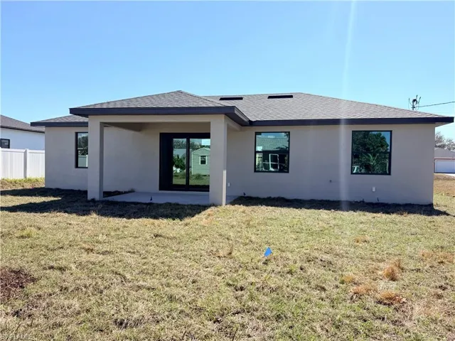 Rear view of property with a shingled roof, stucco siding, and a patio