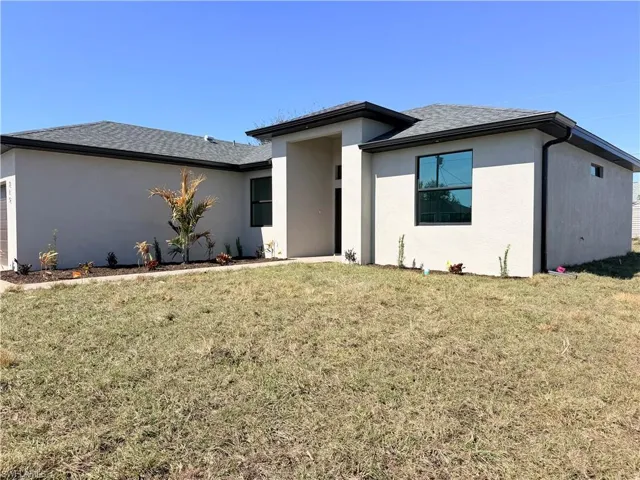 View of front facade featuring a front yard, stucco siding, roof with shingles, and a garage
