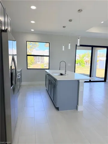 Kitchen with stainless steel appliances, decorative light fixtures, light stone counters, a center island with sink, and light tile patterned flooring