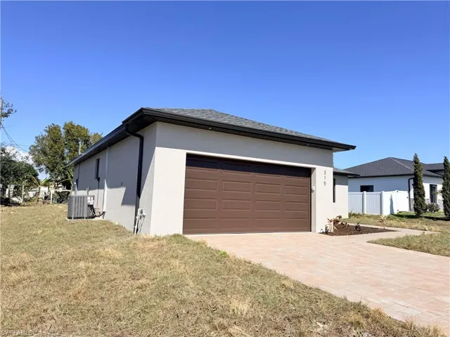 View of side of property with stucco siding, decorative driveway, a lawn, and a garage