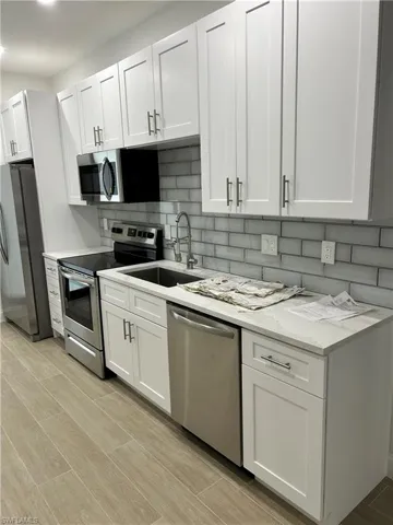 Kitchen with light hardwood / wood-style floors, decorative backsplash, light stone countertops, white cabinets, and appliances with stainless steel finishes