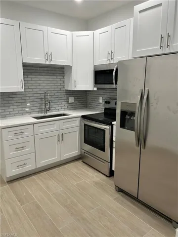 Kitchen with sink, white cabinetry, light hardwood / wood-style flooring, appliances with stainless steel finishes, and backsplash