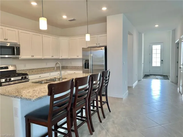 Kitchen with light stone counters, appliances with stainless steel finishes, a kitchen bar, pendant lighting, and white cabinets