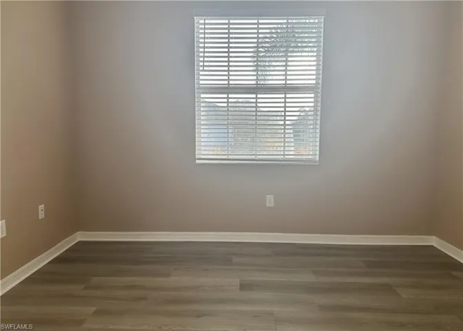 Empty room featuring dark wood-style flooring and baseboards