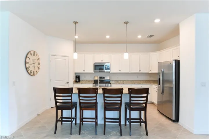 Kitchen with appliances with stainless steel finishes, a kitchen bar, decorative light fixtures, white cabinets, and light stone countertops