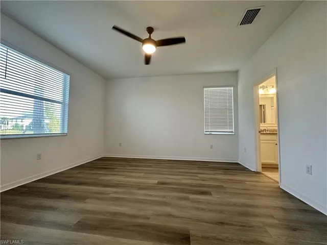Unfurnished bedroom featuring dark wood finished floors, ceiling fan, and ensuite bath