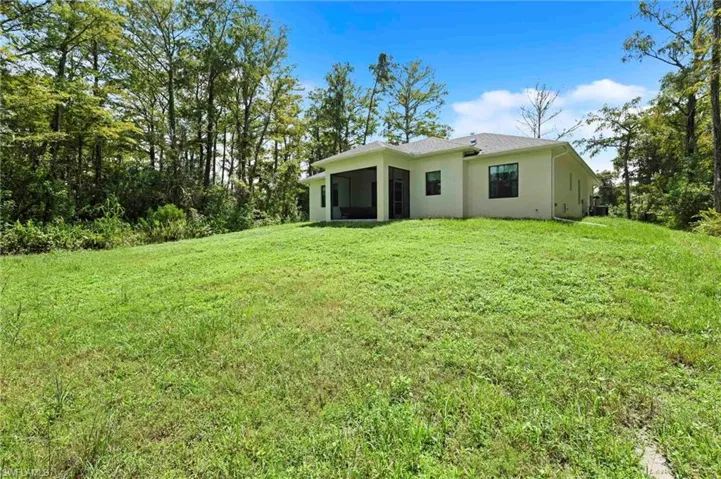 Expansive rear yard with a sloped landscape and mature trees
