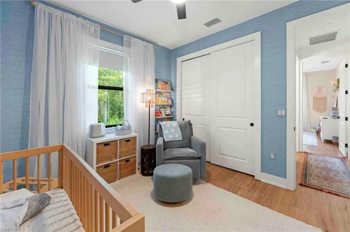 Light wood-finish flooring, full-height window with white sheer curtains, built-in closet with sliding doors, ceiling fan, and textured wall finish