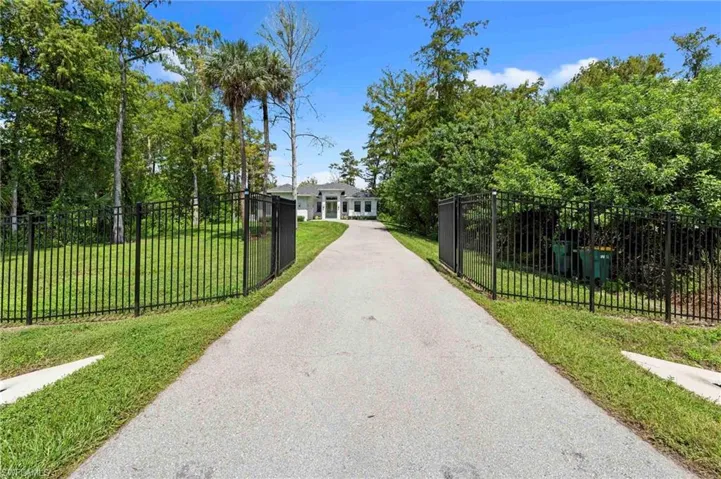 Gated entry with a paved driveway, surrounded by lush landscaping and mature trees