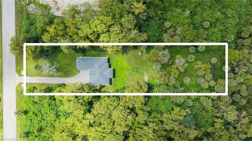 Expansive rectangular lot featuring a detached residential structure, lush green landscaping, a paved driveway, and mature trees