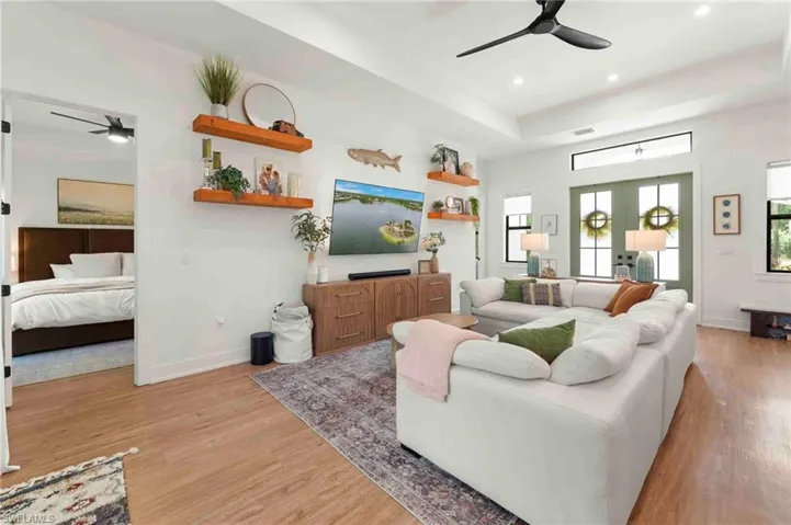 Recessed ceiling lighting, wood-finish flooring, tray ceiling, matte black ceiling fan, and painted French doors