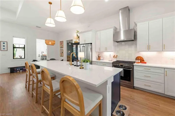 Open-concept kitchen featuring an expansive island with seating, pendant lighting, stainless steel appliances, and wood-finish flooring