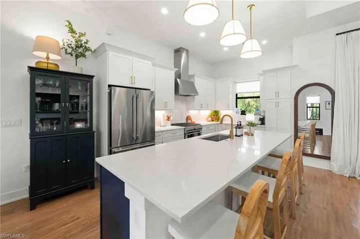 Kitchen featuring white cabinetry, stainless steel appliances, a large center island with a sink, and pendant lighting