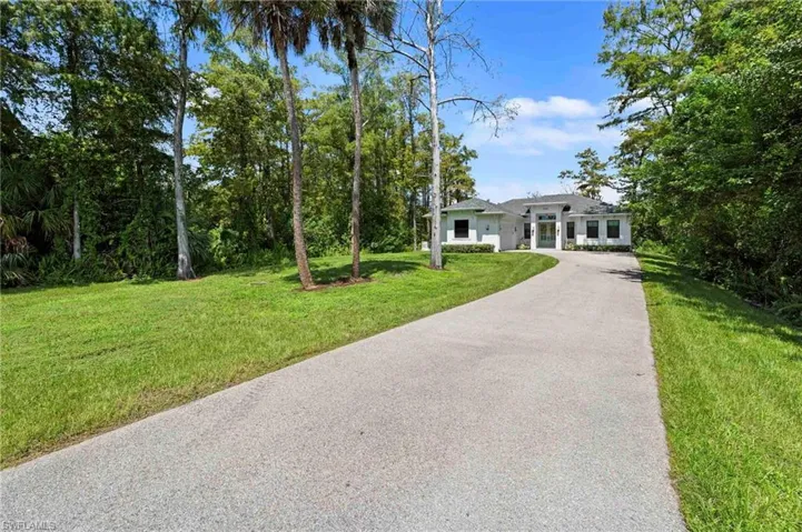 Paved driveway with lush green lawn, mature trees, and a contemporary white exterior