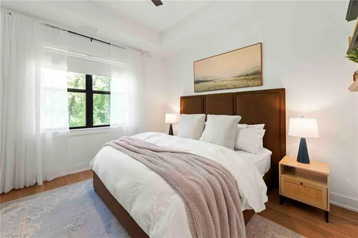 Recessed ceiling with a ceiling fan, wood-finish flooring, and a large window with white sheer drapery