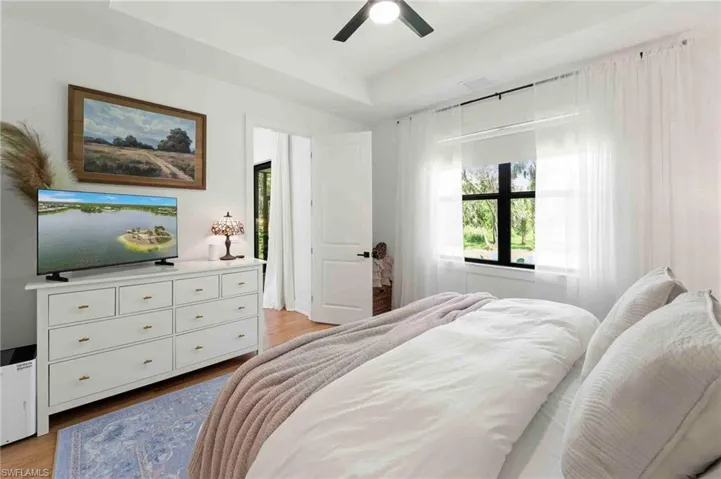 Recessed ceiling, wood-finish flooring, white walls, black window frames, and ceiling fan with integrated lighting