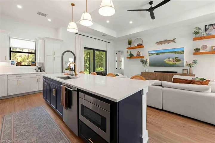 White shaker cabinetry with gold-tone hardware, large kitchen island with integrated sink, stainless steel built-in microwave, wood-finish flooring, and recessed lighting