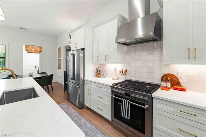Gourmet kitchen with stainless steel appliances, white cabinetry, solid surface countertops, a tile backsplash, and wood-finish flooring
