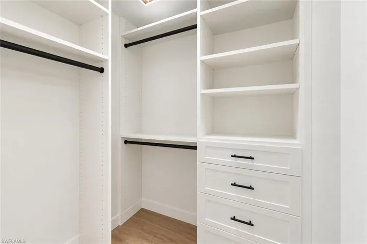 Custom closet system with white cabinetry, integrated shelving, three pull-out drawers with matte black hardware, and multiple hanging rods