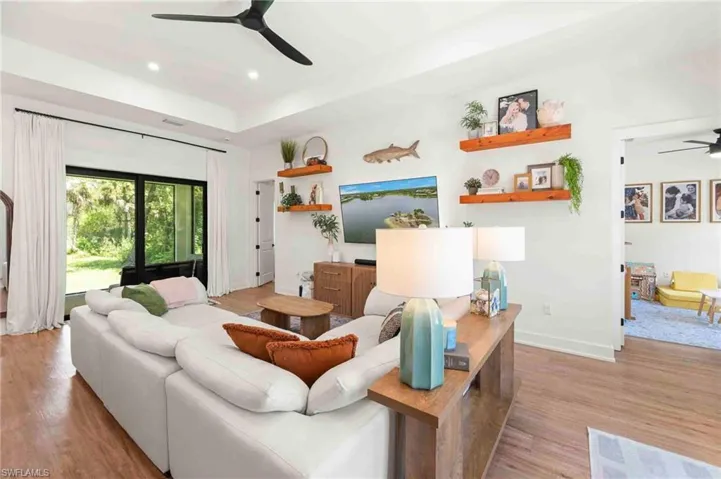 Tray ceiling, wood-finish flooring, glass sliding doors, recessed lighting, and a contemporary ceiling fan