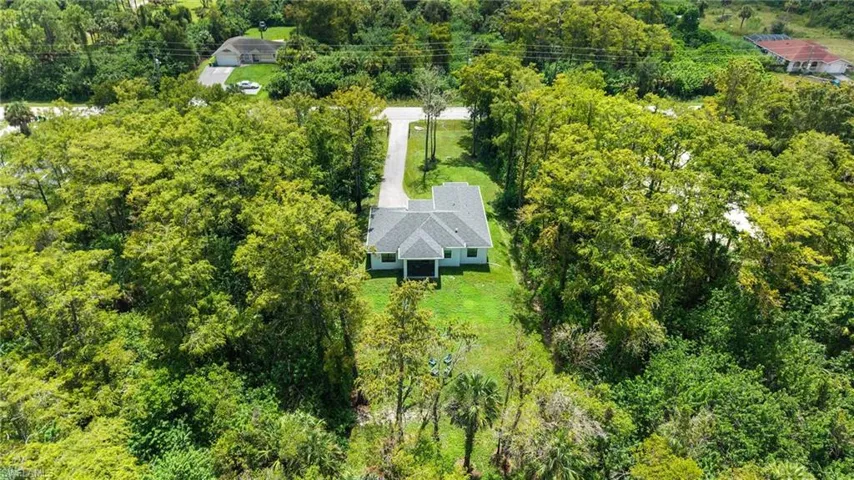 Single-story residence with a gray shingle roof, surrounded by extensive mature trees and green landscaping