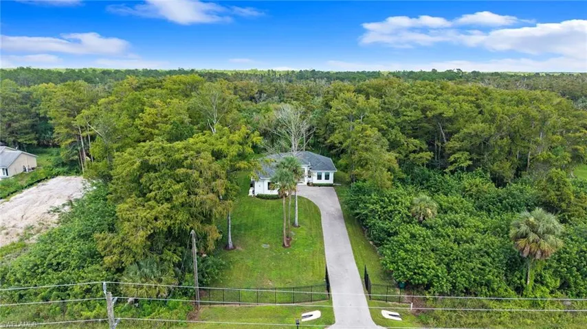 Paved driveway leading to a single-story residence, surrounded by mature trees and natural landscaping