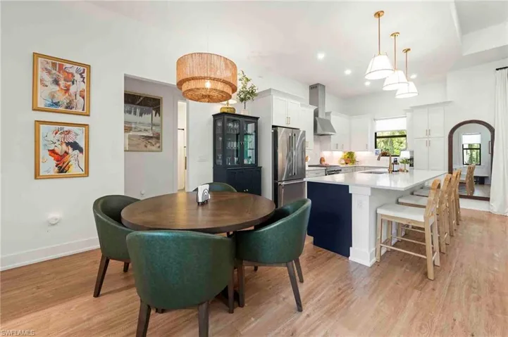 Wood-finish flooring, white cabinetry, stainless steel appliances, a large center island with seating, and recessed lighting