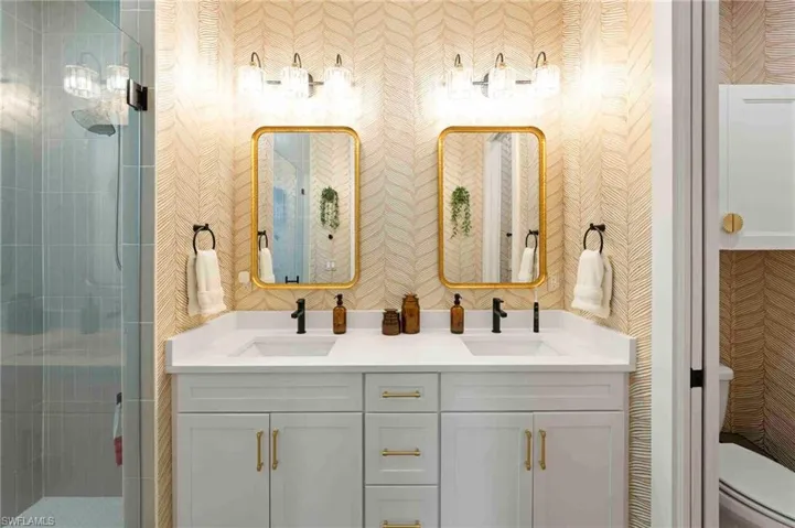 Dual vanity with white shaker-style cabinetry, matte black fixtures, and gold-framed mirrors