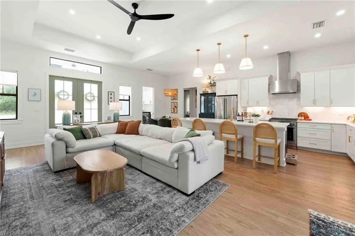 Vaulted ceilings with recessed lighting, wood-finish flooring, white kitchen cabinetry, stainless steel appliances, and a kitchen island with pendant lighting