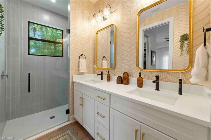 Dual vanity with white cabinetry and gold hardware, matte black faucets, and rectangular mirrors with gold frames