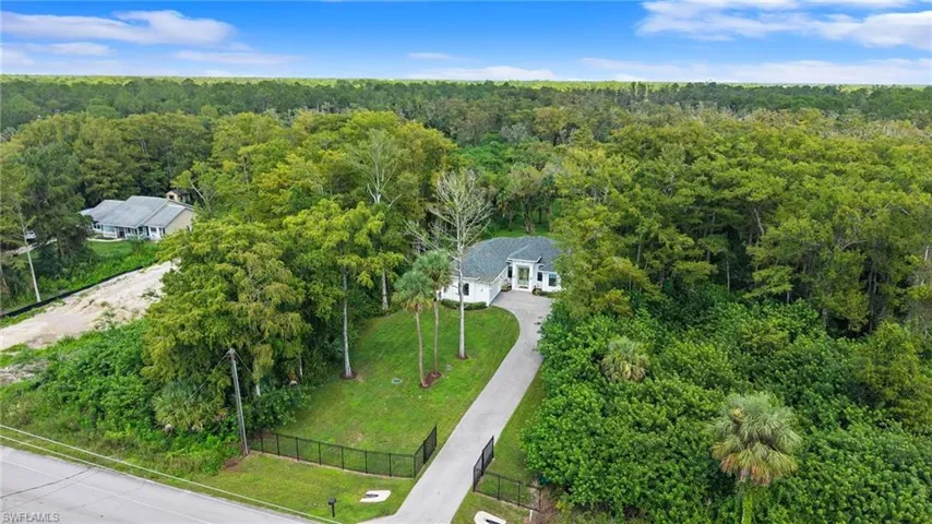 Gated property entry with a paved driveway, surrounded by extensive mature landscaping and a dense tree line