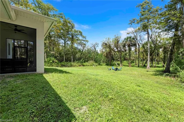 Expansive green space featuring mature trees and a screened-in porch with a ceiling fan, providing a private outdoor living area