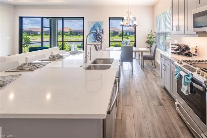 Kitchen with light hardwood / wood-style flooring, appliances with stainless steel finishes, decorative light fixtures, backsplash, and a chandelier