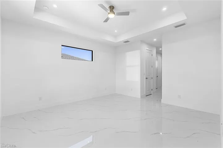 Unfurnished room featuring a tray ceiling, recessed lighting, a ceiling fan, and light marble finish floors