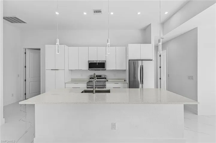 Kitchen with appliances with stainless steel finishes, light stone countertops, white cabinetry, a center island with sink, and hanging light fixtures