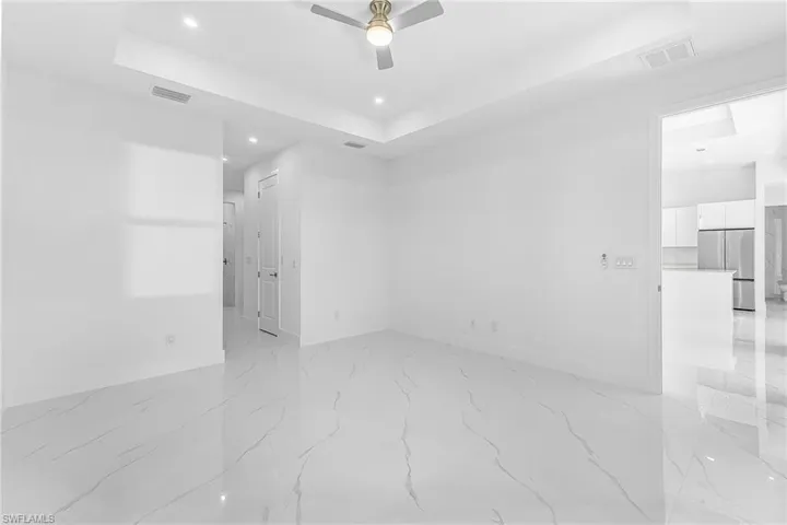Empty room with a raised ceiling, recessed lighting, a ceiling fan, and light marble finish flooring